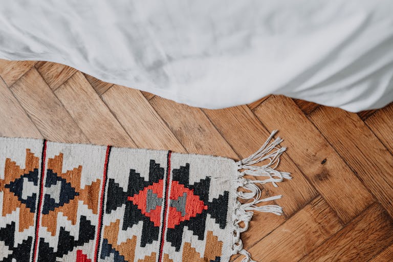 Top view of a cozy bedroom showcasing a colorful patterned rug on a wooden floor and pristine white bed linens.